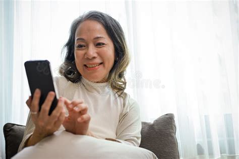 Beautiful Asian Middle Aged Woman In Living Room While Reading Online