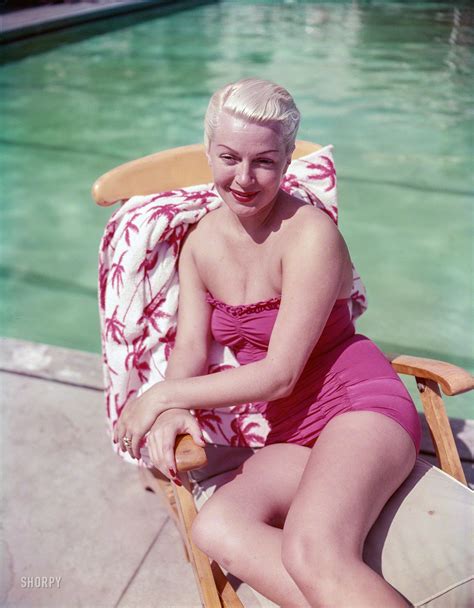 A Woman In A Pink Bathing Suit Sitting On A Wooden Chair Next To A Pool