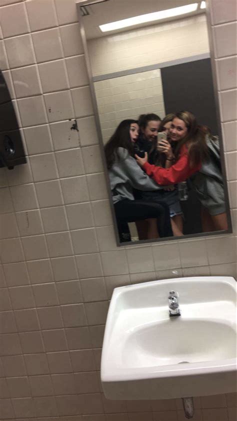 Three Women Taking A Selfie In The Mirror Of A Public Restroom Stall