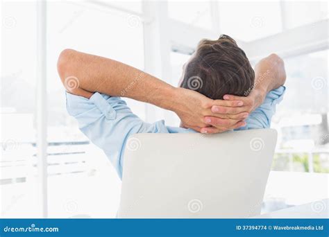 Rear View Of A Casual Man Resting With Hands Behind Head In Office