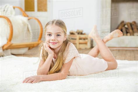 Cute Little Girl Lying On White Carpet And Smiling At Camera Stock