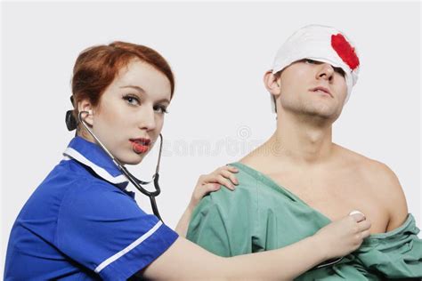 Male Doctor With Female Nurse Bandaging An Injured Patient Against Gray