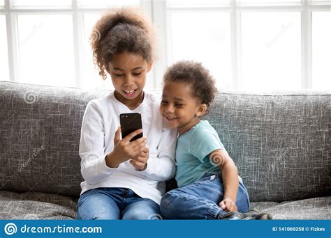Funny Little Black Kids Have Fun Playing On Smartphone Stock Photo