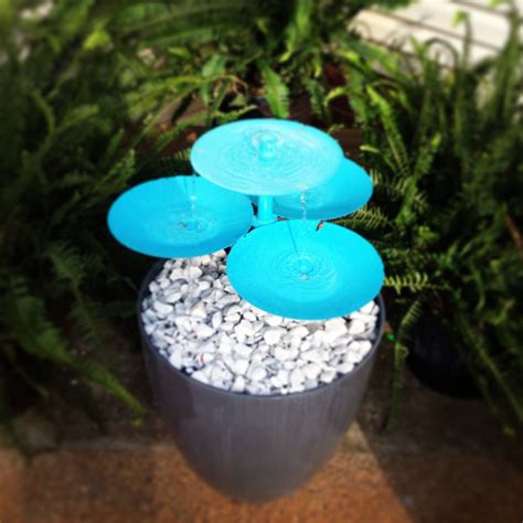 Three Blue Frisbees Sitting On Top Of A Trash Can In Front Of Some Plants