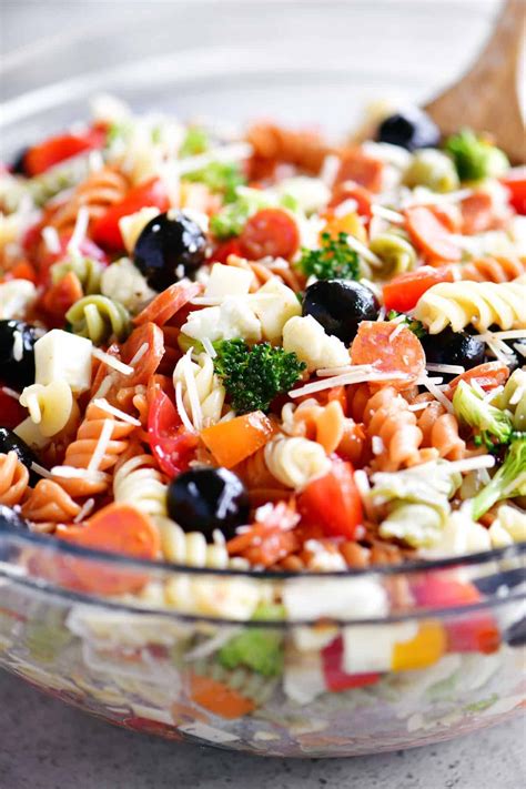A Bowl Filled With Pasta Salad Next To A Wooden Spoon