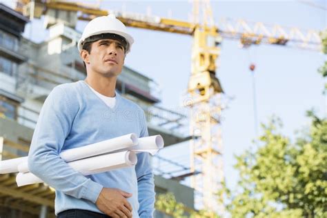 Male Architect Holding Rolled Up Blueprints While Standing At