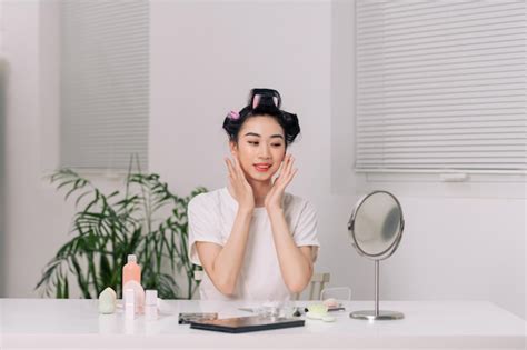 Mulher Muito Asiática Fazendo Massagem Facial Sentada à Mesa No Quarto Olhando Para O Espelho E