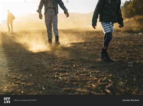Three People Walking Down A Dirt Road Together At Sunset Stock Photo