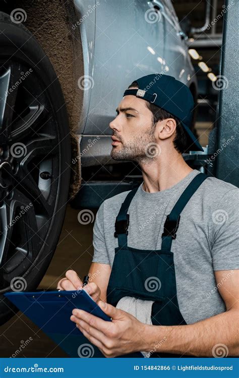Side View Of Concentrated Repairman With Notepad Checking Car Wheels