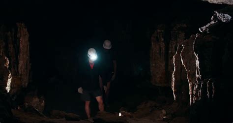 Two Young Men Speleologists With Flashlight Walks In A Dark Cave Stock