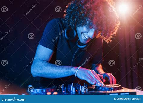Man With Curly Hair Using Dj Equipment And Standing In The Dark Neon