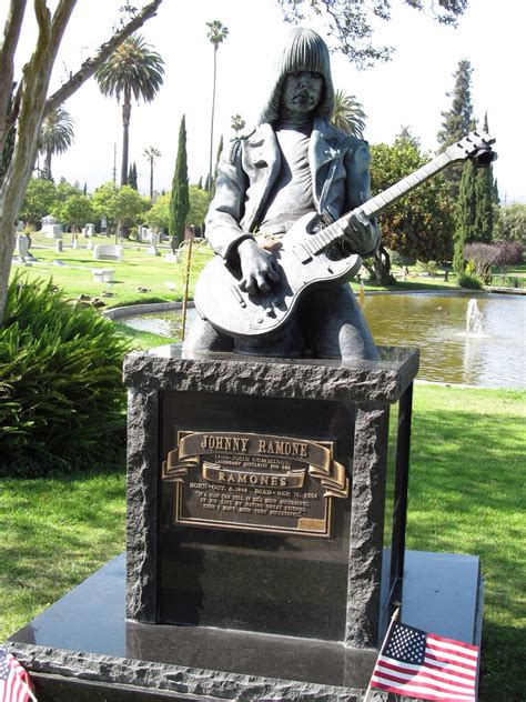 A Statue Of A Person With A Guitar In Front Of A Pond And American Flag