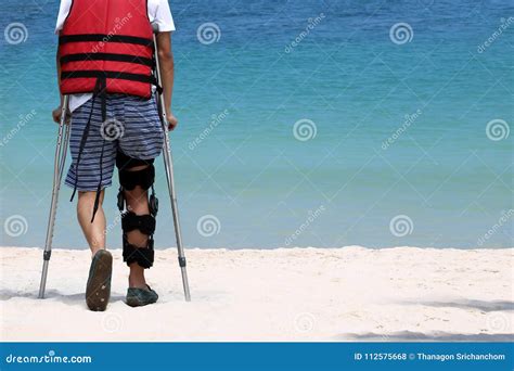 Disabled Man With Crutches While Travel On The Beach Stock Photo