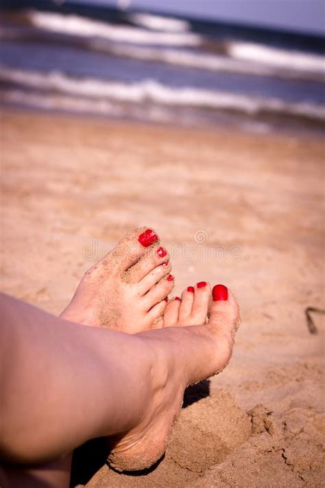 Feet Of Woman With Nails Painted Red On The Sand Of The Sea Stock Photo