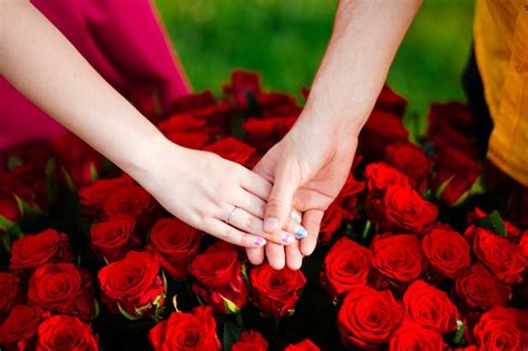 premium photo couple in love holding hands over a bouquet of red roses