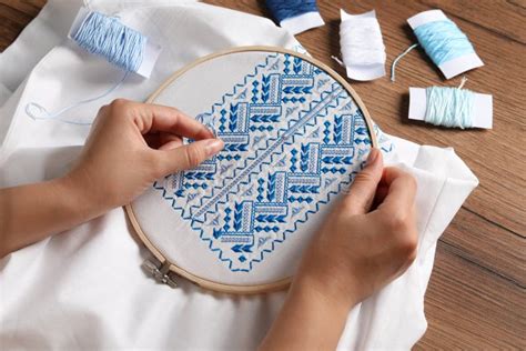 Woman Embroidering White Shirt With Blue Thread At Wooden Table Above