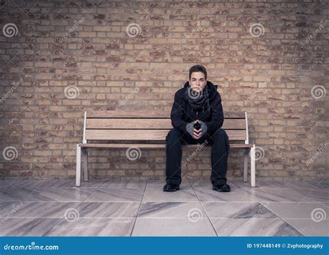 Young Man Sitting On Bench With Brick Wall In Background Stock Image