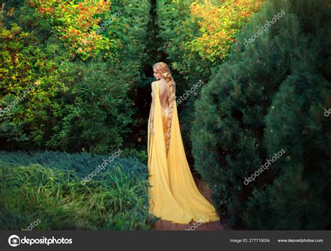 slender beauty in elegant bright dress with stretching trains goes to thick of magical garden