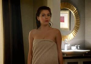 A Woman In A Towel Standing In Front Of A Bathroom Sink And Looking At