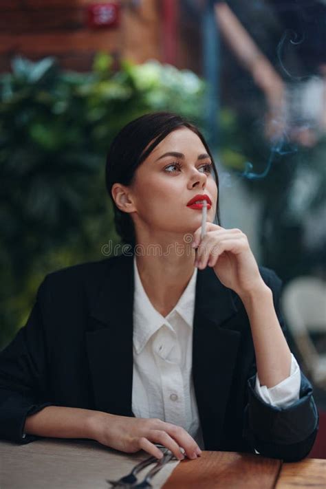 Stylish Fashion Woman Portrait Sitting In A Cafe At A Table And Smoking