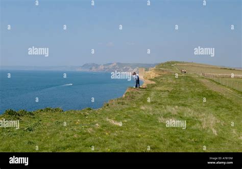 Two Walkers Peering Over Cliff Edge Along The Southwest Coast Path At