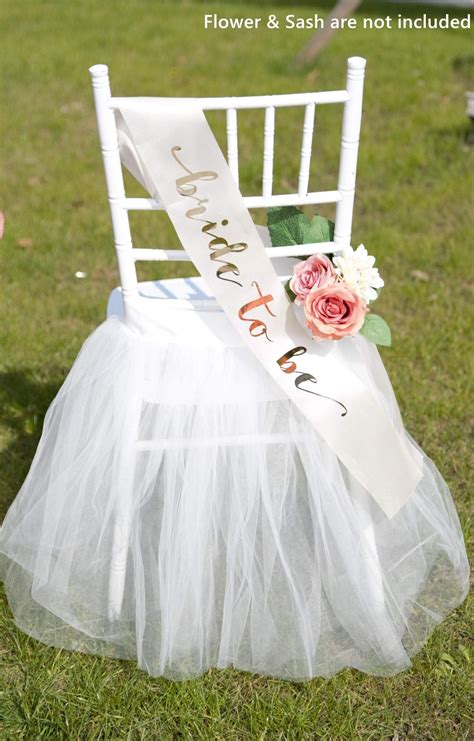 A White Chair With A Flower And Sash On It Sitting In The Grass Next To