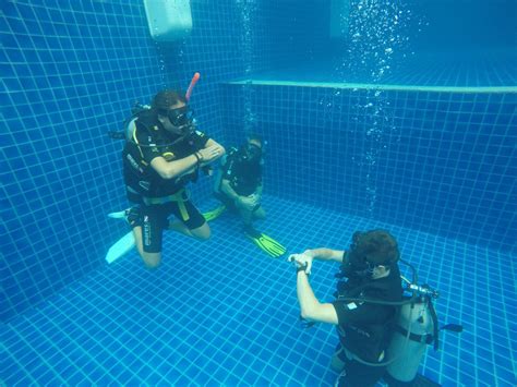Two People In Scuba Gear Standing Next To Each Other Near A Blue Tiled Wall And Floor