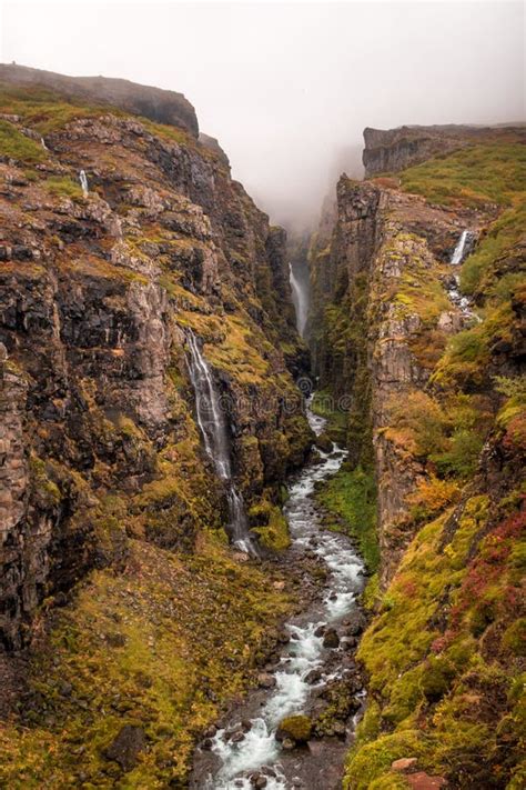 Vertical Picture Of The Glymur Waterfall Surrounded By Rocks Covered In