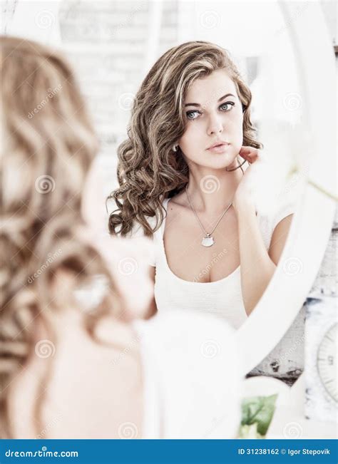 Young Beautiful Woman Looking At Her Face In The Mirror Stock Photo