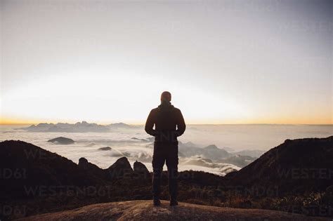 Rear View Of Man Standing On Mountain During Sunset Stock Photo
