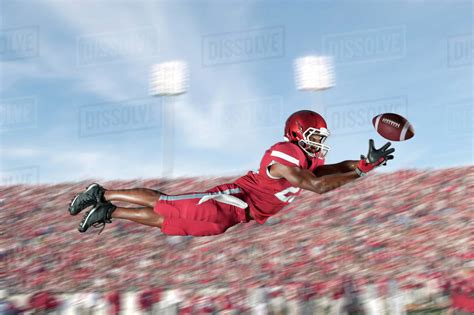 African American Football Player Jumping In Mid Air Catching Football