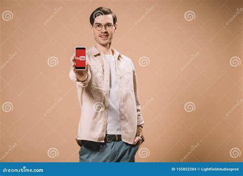 Cheerful Man Standing With Hand In Pocket And Holding Smartphone With