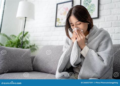 Sick Young Asian Woman Sitting Under The Blanket On Sofa And Sneeze
