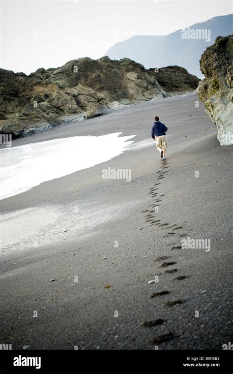 Man Alone Walking Away On The Beach Leaving A Trail Of Footprints In