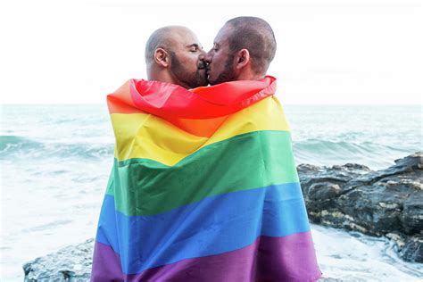 lgbt pride concept gay couple embracing lovingly wrapped in the rainbow flag photograph by