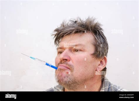 Portrait Of A Weirdo Holding A Blue Syringe In His Mouth Unshaven Man