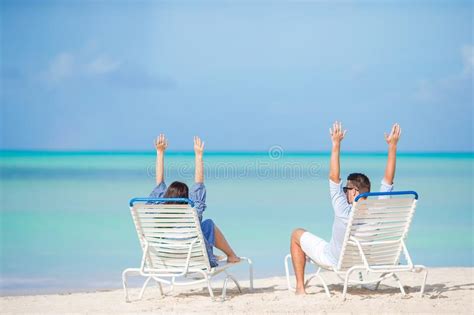 Two Happy People Having Fun On The Beach Sitting On Comfortable Sunbed