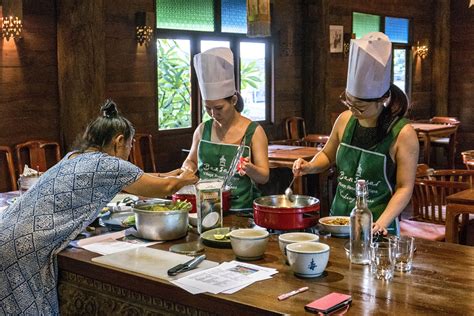 Three Women In Green Aprons Preparing Food On A Wooden Kitchen Table