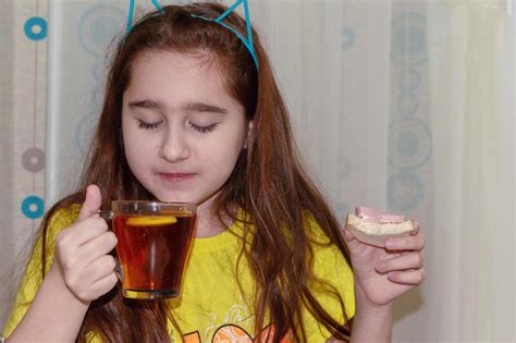 una adolescente está sentada en una mesa en la cocina y toma té con un sándwich mañana