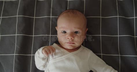 Little Newborn Baby Boy Lies On A Bed On His Back Looking At Camera