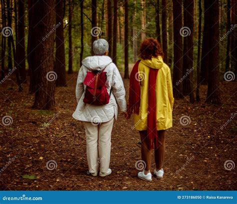 Two Old Female Friends Hiking Together Through The Forest In Autumn