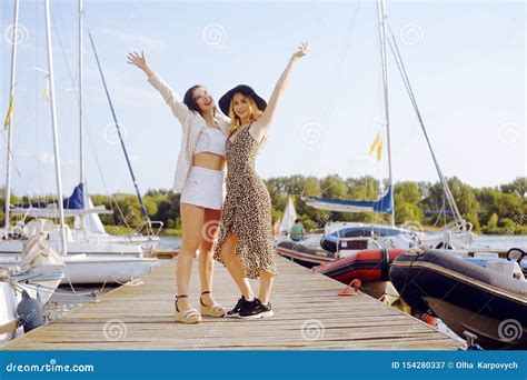 Two Girls On The Background Of Yachts Sailing Boats Are Smiling Looking At The Camera