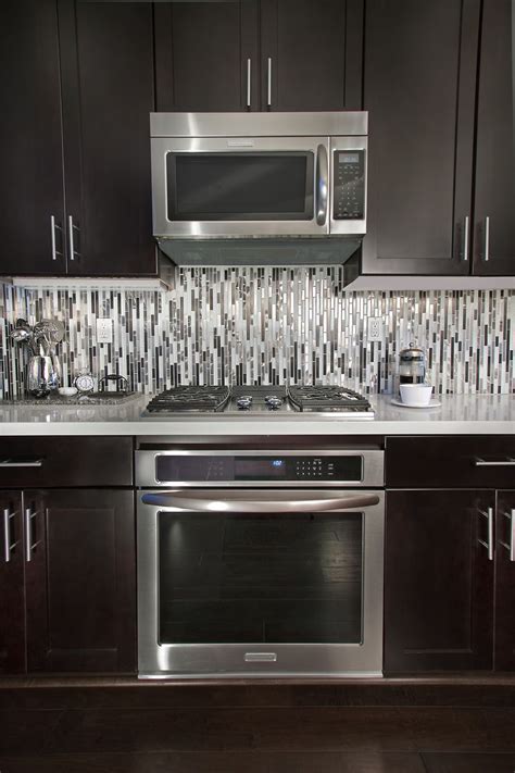 A kitchen backsplash made of all glass tiles is bound to reflect light, and hence brighten up dark spaces under the cabinets. To accentuate the modern lines within we laid the quartz ...