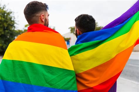 pareja gay envuelta en banderas lgbt de pie atrás foto gratis