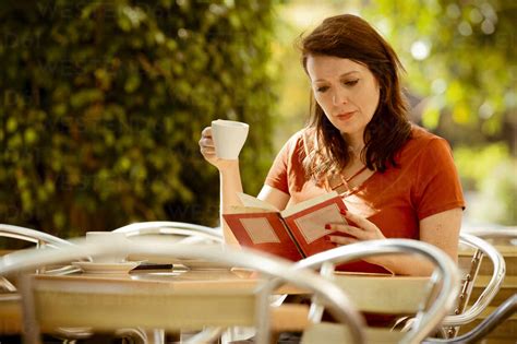 Adult Tranquil Concentrated Lady Reading Book And Drinking Tea While