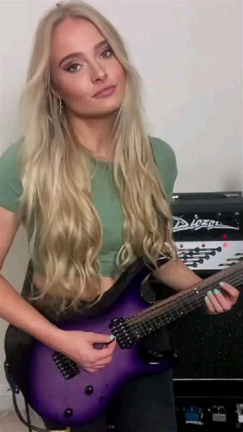 A Woman With Long Blonde Hair Is Holding A Purple Guitar And Posing For