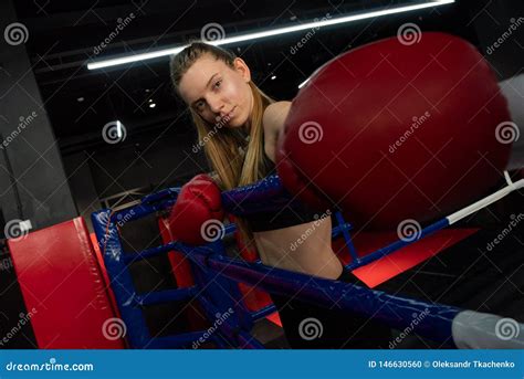 blonde caucasian fighter girl in red boxing gloves is posing on fight club boxing ring stock