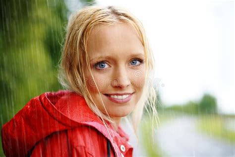 Gorgeous Young Blonde Woman Wearing A Red Raincoat In The Rain Outdoors On A Country Road Stock