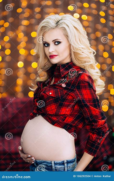 Beautiful And Stylish Pregnant Caucasian Woman In T Shirt And Blue Jeans With Blond Hair Holds