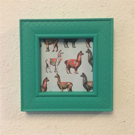 A Green Frame With Llamas On It Hanging On The Wall Next To A White Wall